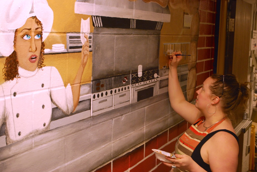 Alecia McClain working on the centerpiece of her recent addition to the cafeteria mural. REID HARMAN|THE HARBINGER