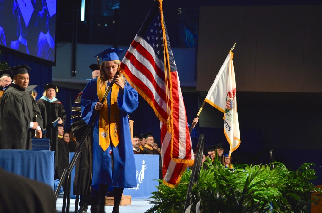 Commencement marshal and graduating student Megan Small carries the American Flag to lead the staff, faculty and graduates out of the gymnasium to mark the end of commencement. REID|HARBINGER